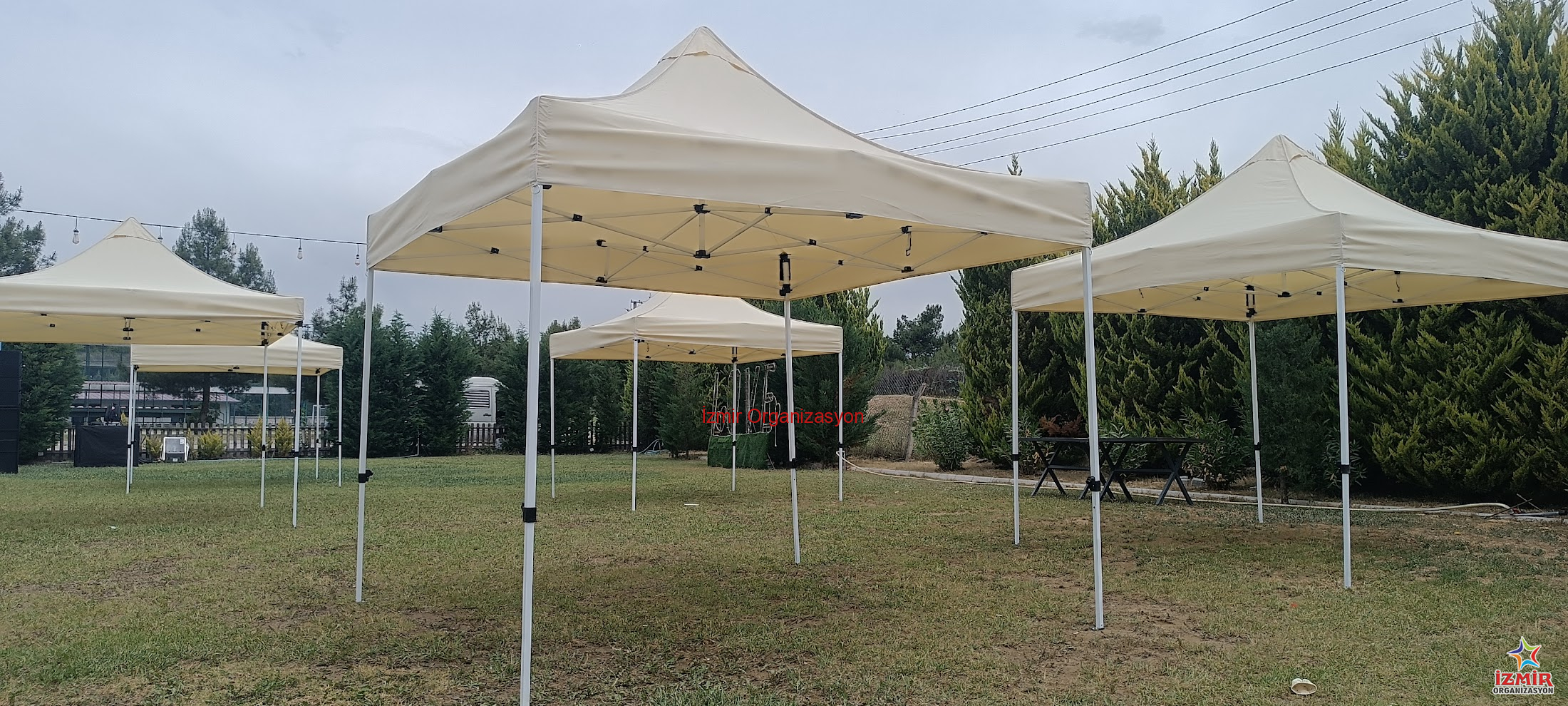 Gazebo Gölgelik Çadır Kiralama auto draft İzmir Organizasyon İzmir'deki açık hava etkinliklerinizde misafirlerinizi güneşten ve hafif yağmurdan korumak için 3x3 Metre Beyaz Gazebo Çadır Kiralama hizmetimizden yararlanın. Toplamda 9 m² gölgelik alan sunan bu şık çadırlar, 2.5 metre tepe yüksekliği ile ferah bir kullanım sağlar. Görselde görüldüğü gibi yan yana kurularak uzun koridorlar veya geniş gölgelik adalar oluşturulabilir. Kermesler, bahçe partileri, fuar stantları, piknik organizasyonları ve dış mekan kayıt masaları için idealdir. Beyaz rengiyle her türlü dekorasyona uyum sağlar, temiz ve profesyonel bir görüntü sunar. Kurulum ve toplama işlemi ekibimiz tarafından yapılmaktadır. Stok durumu ve nakliye planlaması için bizimle iletişime geçebilirsiniz. İzmir Beyaz 3x3 Gazebo Çadır Kiralama