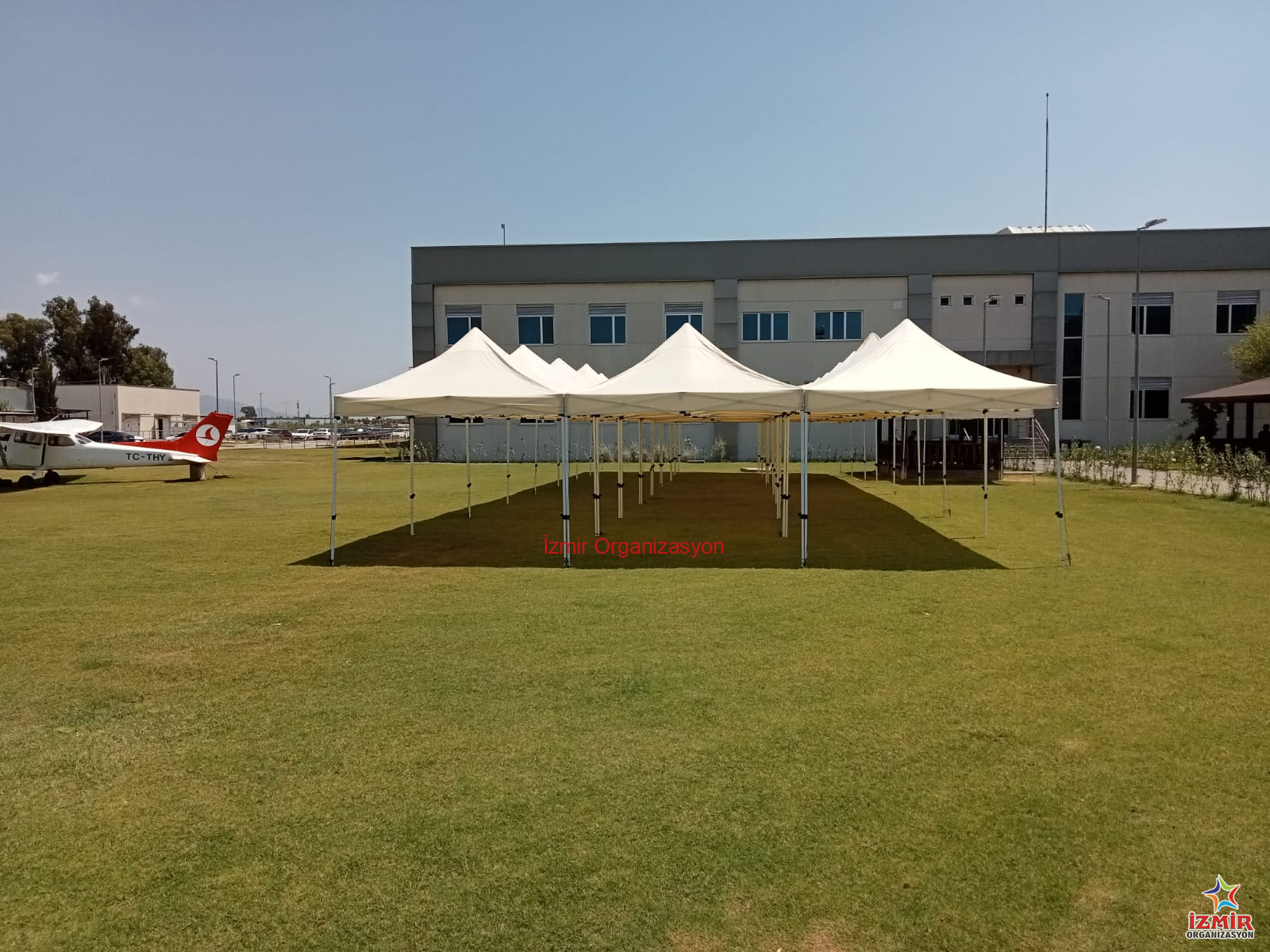 Gazebo Gölgelik Çadır Kiralama gazebo golgelik cadir kiralama 1 İzmir Organizasyon İzmir'deki açık hava etkinliklerinizde misafirlerinizi güneşten ve hafif yağmurdan korumak için 3x3 Metre Beyaz Gazebo Çadır Kiralama hizmetimizden yararlanın. Toplamda 9 m² gölgelik alan sunan bu şık çadırlar, 2.5 metre tepe yüksekliği ile ferah bir kullanım sağlar. Görselde görüldüğü gibi yan yana kurularak uzun koridorlar veya geniş gölgelik adalar oluşturulabilir. Kermesler, bahçe partileri, fuar stantları, piknik organizasyonları ve dış mekan kayıt masaları için idealdir. Beyaz rengiyle her türlü dekorasyona uyum sağlar, temiz ve profesyonel bir görüntü sunar. Kurulum ve toplama işlemi ekibimiz tarafından yapılmaktadır. Stok durumu ve nakliye planlaması için bizimle iletişime geçebilirsiniz. piknik organizasyonu çadır kiralama Bahçe Partisi ve Düğün Gölgelik Kiralama