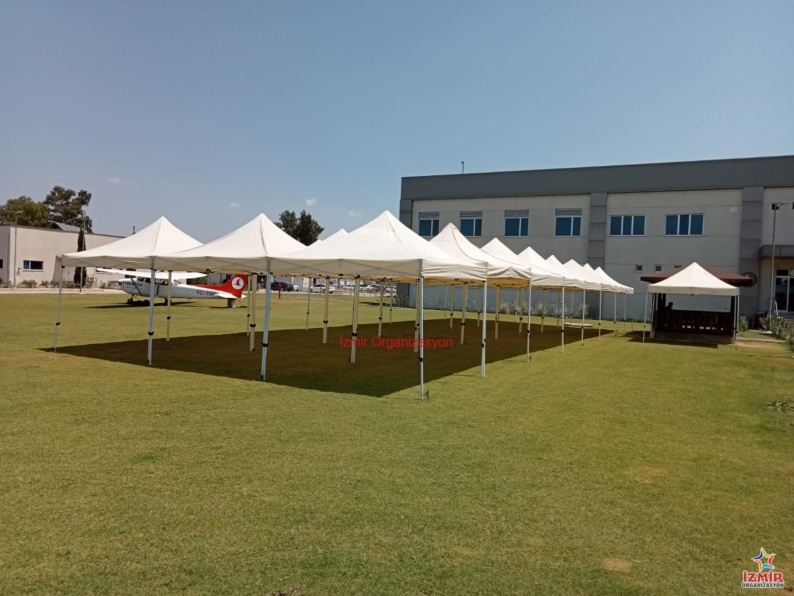 Gazebo Gölgelik Çadır Kiralama gazebo golgelik cadir kiralama İzmir Organizasyon İzmir'deki açık hava etkinliklerinizde misafirlerinizi güneşten ve hafif yağmurdan korumak için 3x3 Metre Beyaz Gazebo Çadır Kiralama hizmetimizden yararlanın. Toplamda 9 m² gölgelik alan sunan bu şık çadırlar, 2.5 metre tepe yüksekliği ile ferah bir kullanım sağlar. Görselde görüldüğü gibi yan yana kurularak uzun koridorlar veya geniş gölgelik adalar oluşturulabilir. Kermesler, bahçe partileri, fuar stantları, piknik organizasyonları ve dış mekan kayıt masaları için idealdir. Beyaz rengiyle her türlü dekorasyona uyum sağlar, temiz ve profesyonel bir görüntü sunar. Kurulum ve toplama işlemi ekibimiz tarafından yapılmaktadır. Stok durumu ve nakliye planlaması için bizimle iletişime geçebilirsiniz. Fuar ve Kermes Stant Çadırları Kiralama