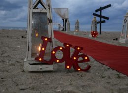 Kuşadası’nda Kumsal Boyu Evlenme Teklifi Organizasyonu İzmir Organizasyon Kuşadası Evlenme Teklifi Organizasyonu Nihal Fatih İzmir Organizasyon Kuşadası'nda evlenme teklifi organizasyonu ile evlilik yolunda ilk adımı atmak isteyen çiftimize özel bir evlilik teklifi organizasyonu hazırladık. Fatih Bey kız arkadaşı Nihal hanım ile olan beraberliklerini, bir ömür boyu yan yana geçirmek istediğine kanaat getirmişti. Nihal hanımla evlilik yolunda ilerlemek istediğine karar veren Fatih bey, peri masalı gibi akıllardan silinmeyecek bir evlenme teklifi organizasyonu yapmak istiyordu. Böyle bir organizasyon için kolları sıvamış ve internetten araştırarak İzmir Organizasyon şirketini bulmuş yani bizimle çalışmaya karar vermişti. Fatih bey ofisimize gelip bizimle görüşürken; kız arkadaşı ile ikisinin de tam bir deniz aşığı olduğunu söyledi ve Kuşadası lokasyonunun hem kendilerine yakın hem de en favori tatil beldesi olduğunu dile getirdi. Dolayısıyla biz de deniz kenarında ve Kuşadası’nda bir evlenme teklifi organizasyonu yapabileceğimiz bahsettik kendisine. Kumsalda romantik bir evlenme teklifi organizasyonu genç çiftimizi için en güzel seçenek olduğuna kanaat getirdik Fatih bey ile. Görüşmemizin ilerleyen dakikalarında Fatih bey ile organizasyonu gerçekleştireceğimiz günü, saati ve çiftimizin en sevdiği şarkıyı kararlaştırdık. Hava şartları da çok önemliydi. Kış aylarında yağmuru ve rüzgarı baz alarak takvimleri inceledik. Hava inceden lodosun hafif kımıltısını gösteriyordu ve durum bu güzel evlenme teklifi organizasyonuna oldukça uygundu. Fatih bey için geriye sadece heyecanla evlilik teklifi organizasyonu yapacağı günü beklemek, ekip arkadaşlarımız için ise her zaman ki gibi kusursuz bir evlenme teklifi organizasyonu hazırlamak kalmıştı. Kuşadası’nda Kumsal Boyu Evlenme Teklifi Organizasyonu İzmir Organizasyon Kuşadası Evlenme Teklifi Organizasyonu Nihal Fatih İzmir Organizasyon