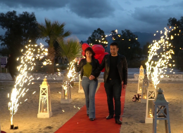 Kuşadası’nda Kumsal Boyu Evlenme Teklifi Organizasyonu İzmir Organizasyon Kuşadası Evlenme Teklifi Organizasyonu Nihal Fatih İzmir Organizasyon Kuşadası'nda evlenme teklifi organizasyonu ile evlilik yolunda ilk adımı atmak isteyen çiftimize özel bir evlilik teklifi organizasyonu hazırladık. Fatih Bey kız arkadaşı Nihal hanım ile olan beraberliklerini, bir ömür boyu yan yana geçirmek istediğine kanaat getirmişti. Nihal hanımla evlilik yolunda ilerlemek istediğine karar veren Fatih bey, peri masalı gibi akıllardan silinmeyecek bir evlenme teklifi organizasyonu yapmak istiyordu. Böyle bir organizasyon için kolları sıvamış ve internetten araştırarak İzmir Organizasyon şirketini bulmuş yani bizimle çalışmaya karar vermişti. Fatih bey ofisimize gelip bizimle görüşürken; kız arkadaşı ile ikisinin de tam bir deniz aşığı olduğunu söyledi ve Kuşadası lokasyonunun hem kendilerine yakın hem de en favori tatil beldesi olduğunu dile getirdi. Dolayısıyla biz de deniz kenarında ve Kuşadası’nda bir evlenme teklifi organizasyonu yapabileceğimiz bahsettik kendisine. Kumsalda romantik bir evlenme teklifi organizasyonu genç çiftimizi için en güzel seçenek olduğuna kanaat getirdik Fatih bey ile. Görüşmemizin ilerleyen dakikalarında Fatih bey ile organizasyonu gerçekleştireceğimiz günü, saati ve çiftimizin en sevdiği şarkıyı kararlaştırdık. Hava şartları da çok önemliydi. Kış aylarında yağmuru ve rüzgarı baz alarak takvimleri inceledik. Hava inceden lodosun hafif kımıltısını gösteriyordu ve durum bu güzel evlenme teklifi organizasyonuna oldukça uygundu. Fatih bey için geriye sadece heyecanla evlilik teklifi organizasyonu yapacağı günü beklemek, ekip arkadaşlarımız için ise her zaman ki gibi kusursuz bir evlenme teklifi organizasyonu hazırlamak kalmıştı. Kumsalda Evlilik Teklifi